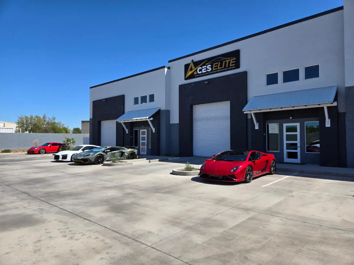 Aces Auto Elite - A row of luxury sports cars, including red and green models, is parked outside a modern building with a CES Elite sign on a clear, sunny day. | Arizona Luxury & Exotic Car Service